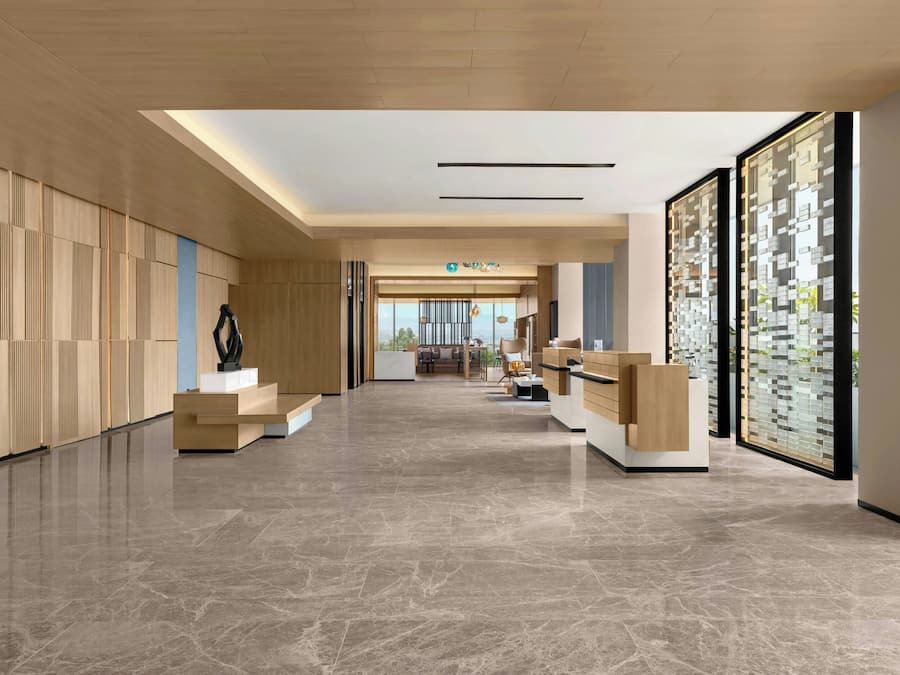 A modern hotel lobby with a marble floor, wooden paneling, and a reception desk.
