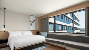 A modern hotel room with a large bed, a seating area, a view of a building, and a large window. - Fairfield By Marriott Cebu Mactan (Lapu-Lapu)