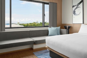 Habitación de hotel moderna con una cama grande, un banco empotrado, vistas de la ciudad y un cuadro en la pared.