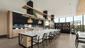 A modern kitchen with a dining area, featuring a long table set for six, wooden cabinets, and pendant lighting. - Fairfield By Marriott Cebu Mactan (Lapu-Lapu)