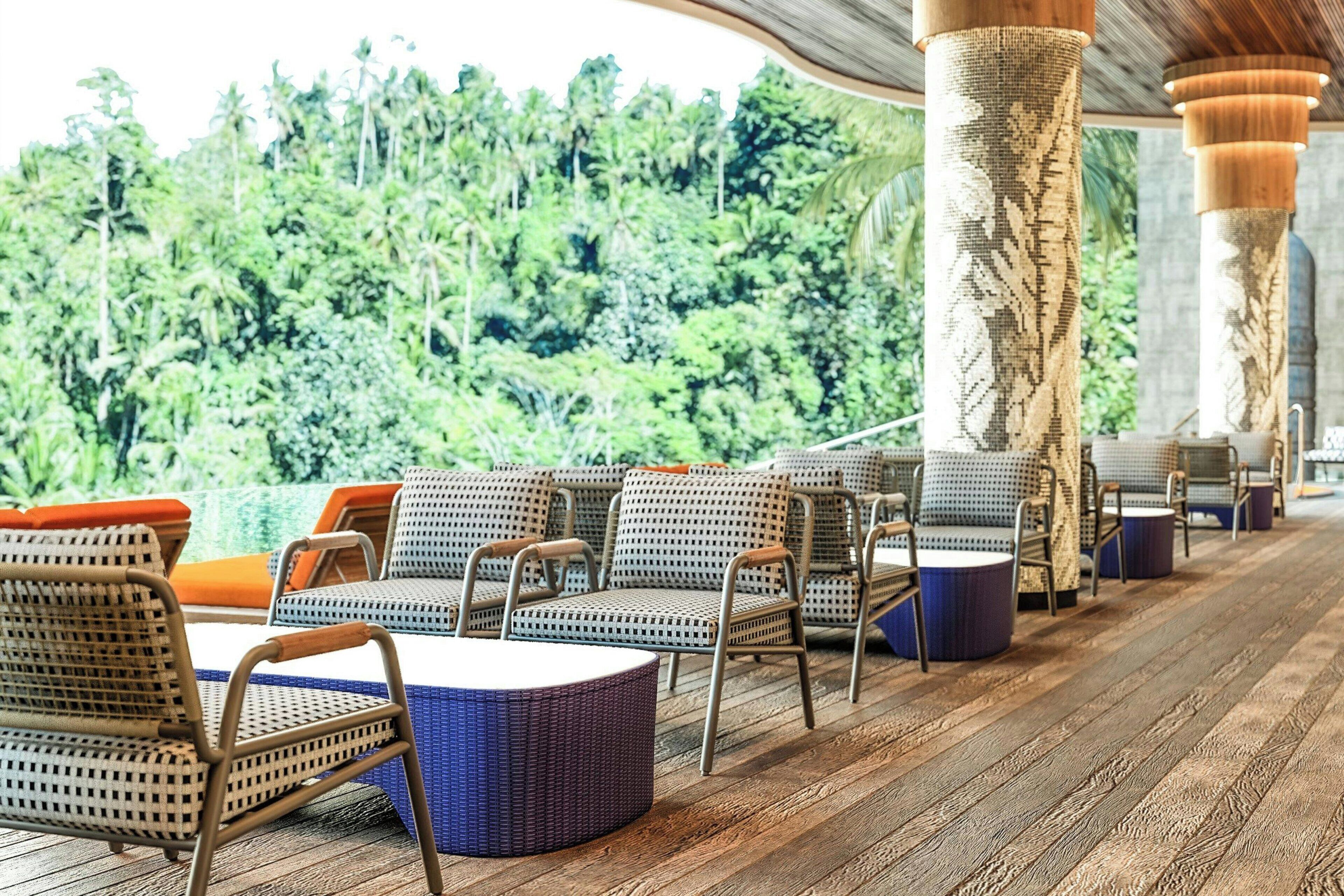 Un espacio de estar al aire libre techado con mobiliario de mimbre y vistas a abundante vegetación.