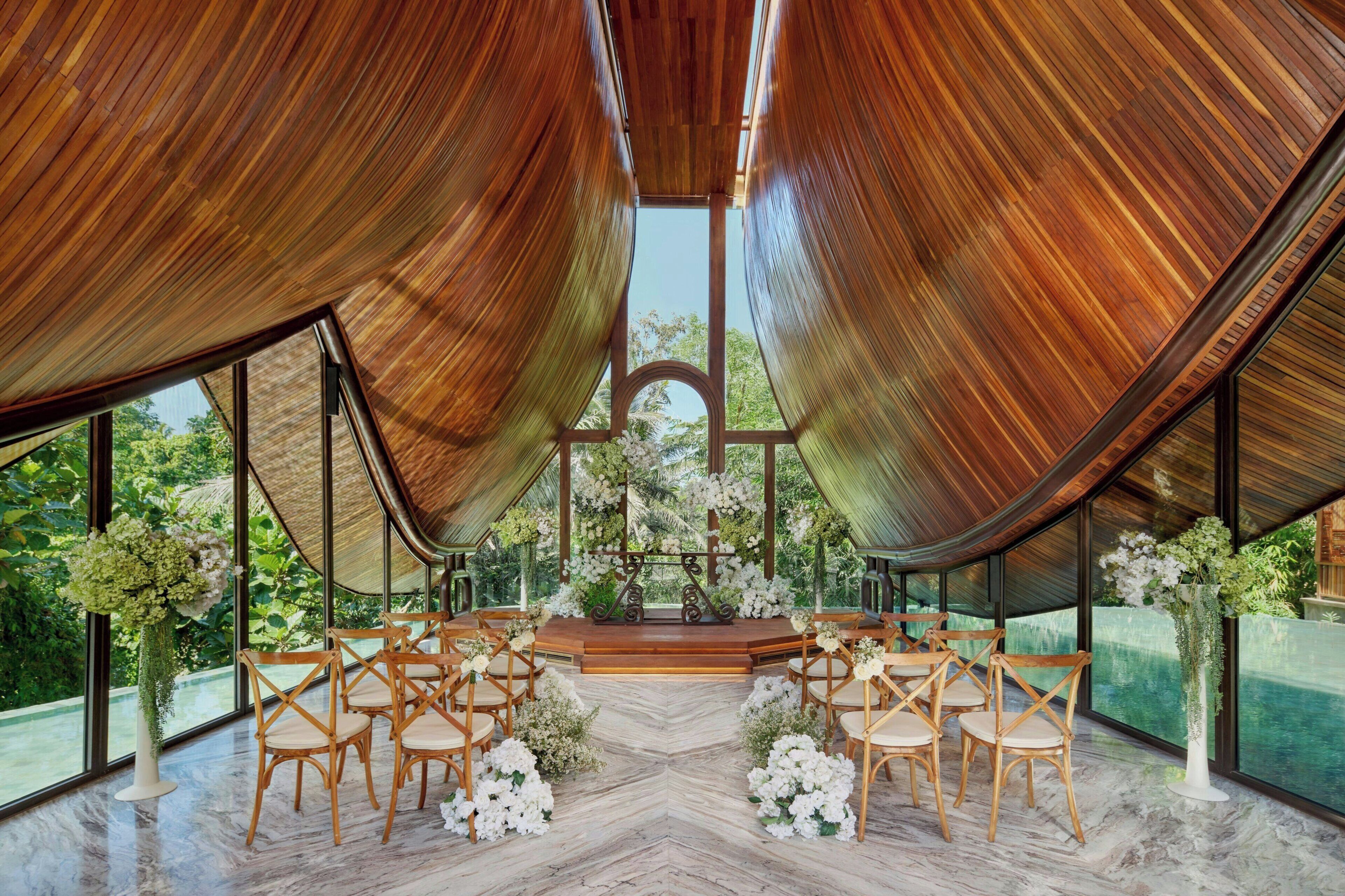 An indoor venue with a wooden ceiling, large windows, and a central stage with floral arrangements.