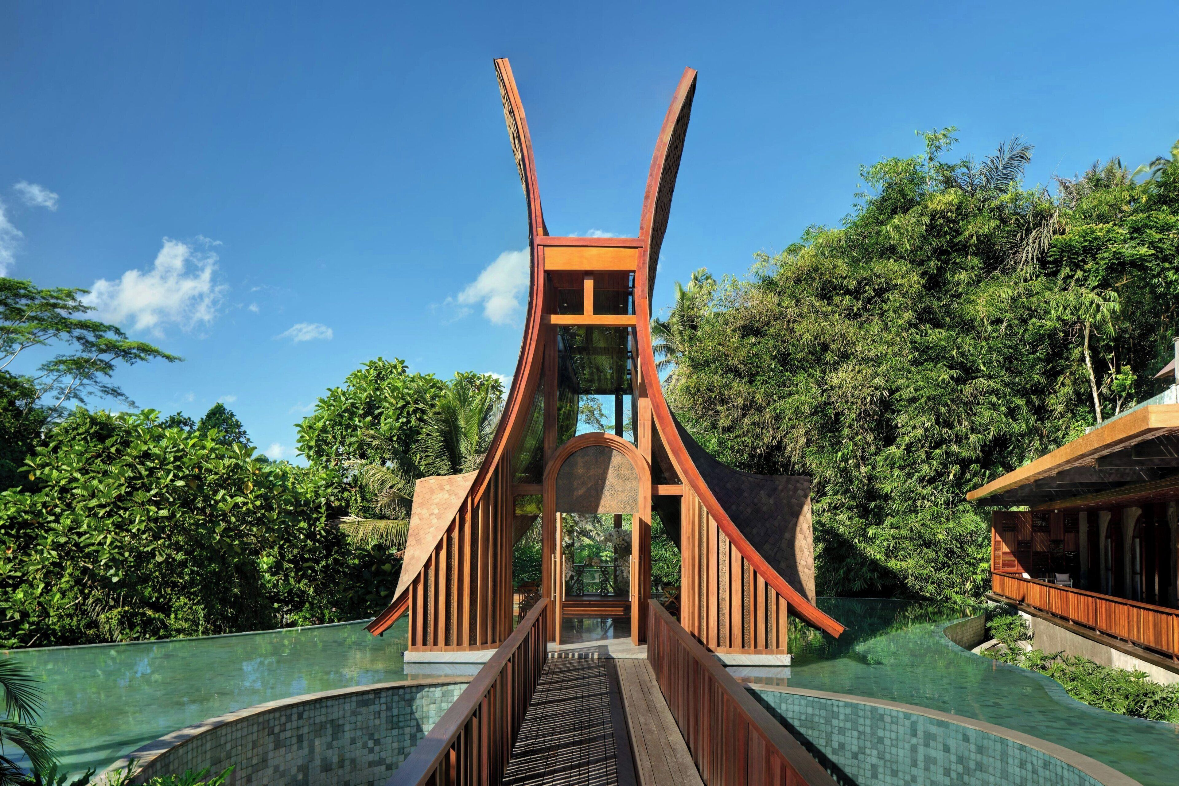 Une structure de pont moderne menant à un espace piscine entouré d’une végétation luxuriante.