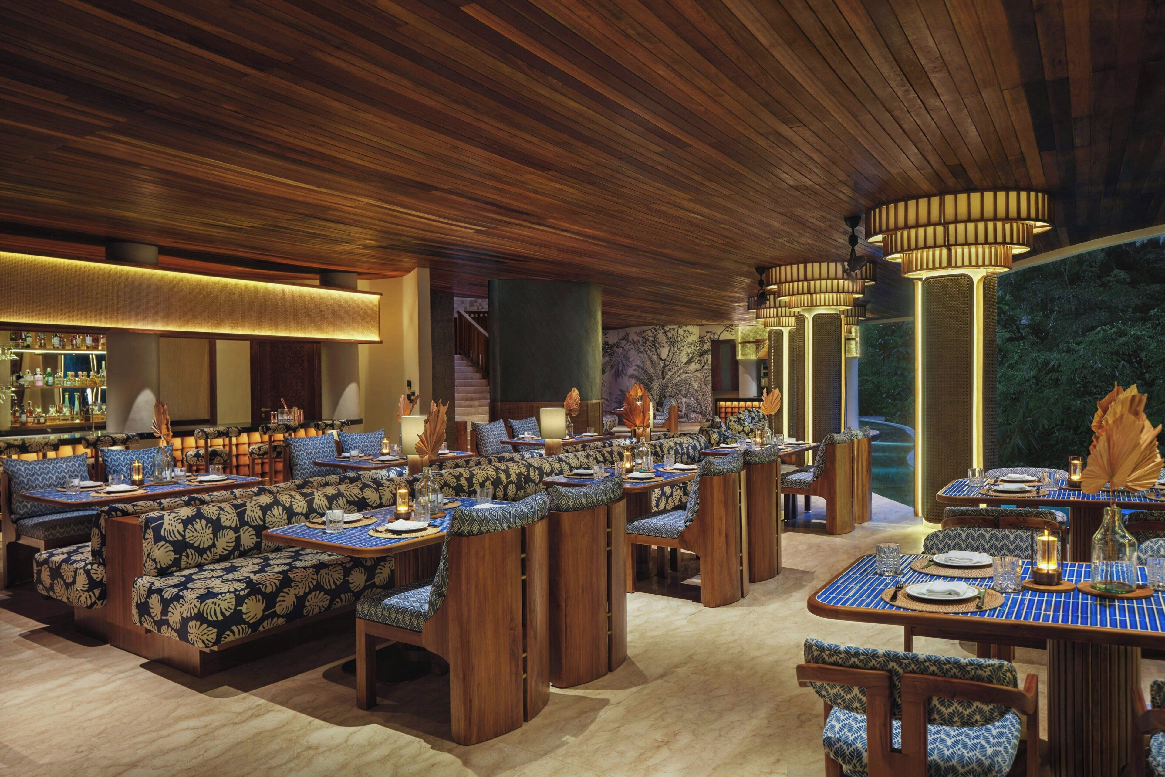 A restaurant with wooden ceiling and walls, patterned seating, and a bar area.
