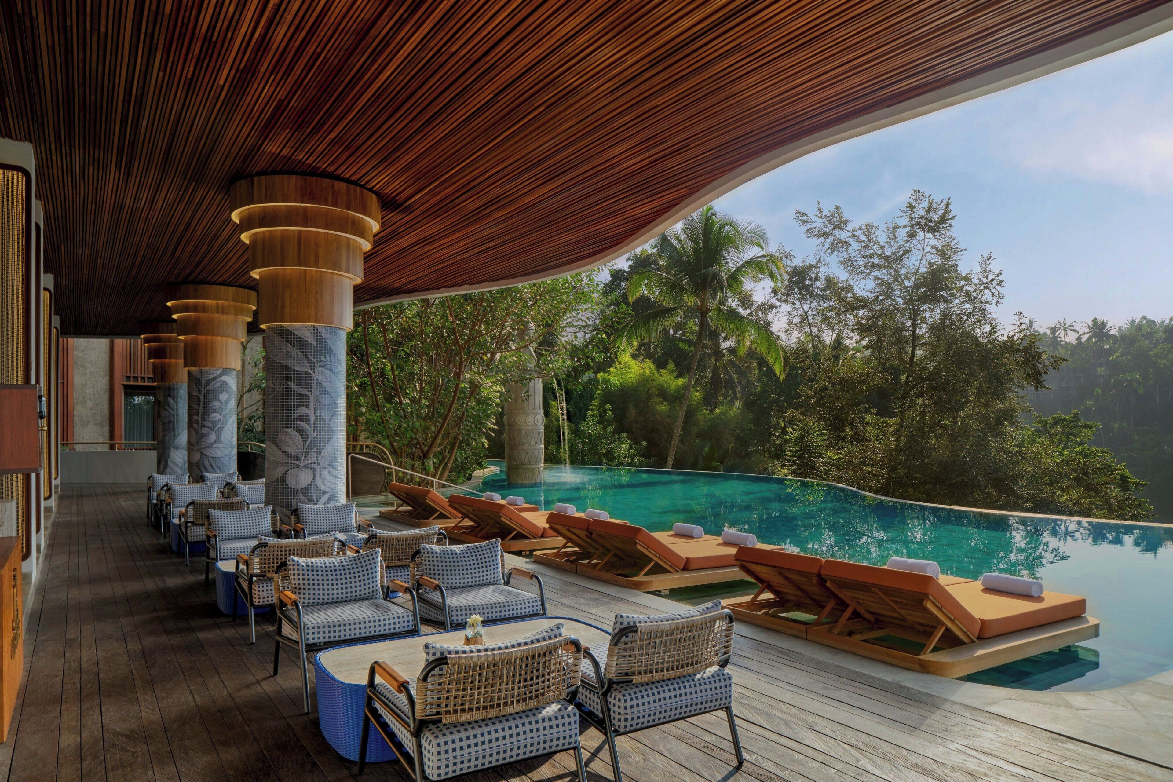 A poolside area with lounge chairs and a view of a pool surrounded by tropical vegetation.