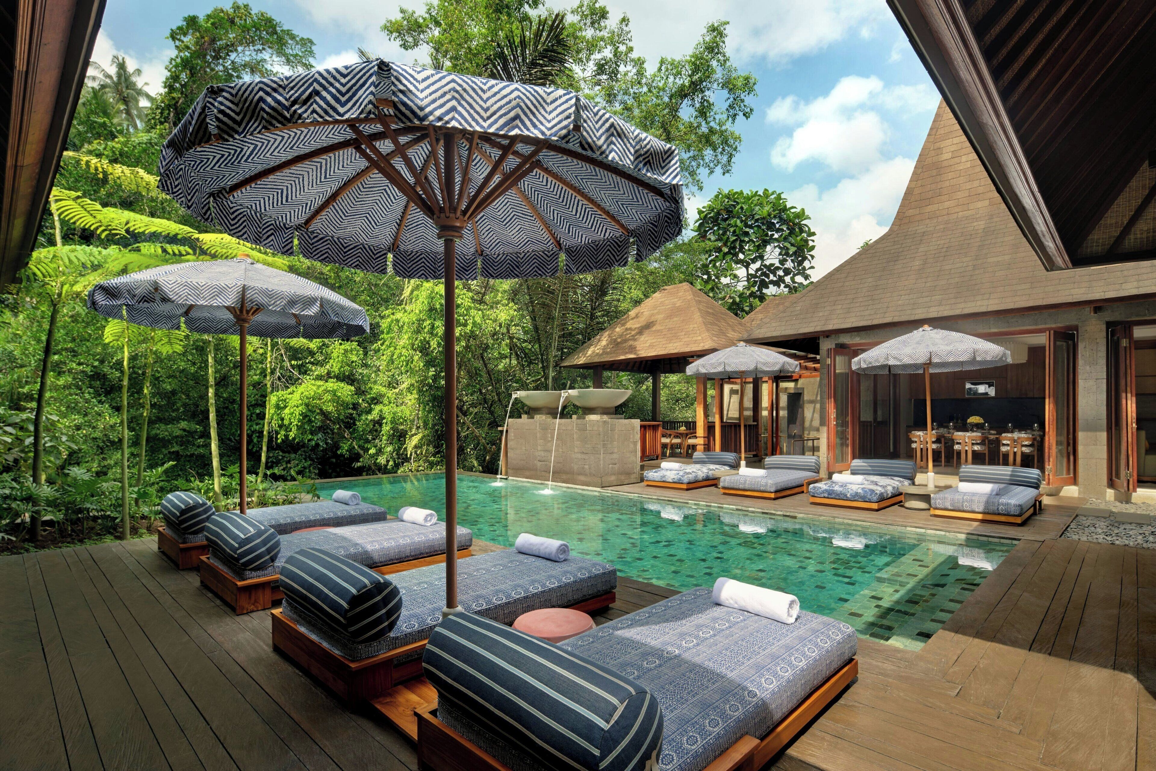A poolside area with lounge chairs and umbrellas, surrounded by lush greenery.