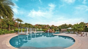 A swimming pool with a waterfall feature, surrounded by palm trees and lounge chairs. - The Westin Jaipur Kant Kalwar Resort And Spa (Amer)