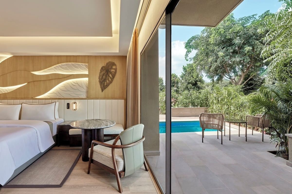 A modern hotel room with a bed, seating area, and a view of an outdoor swimming pool.