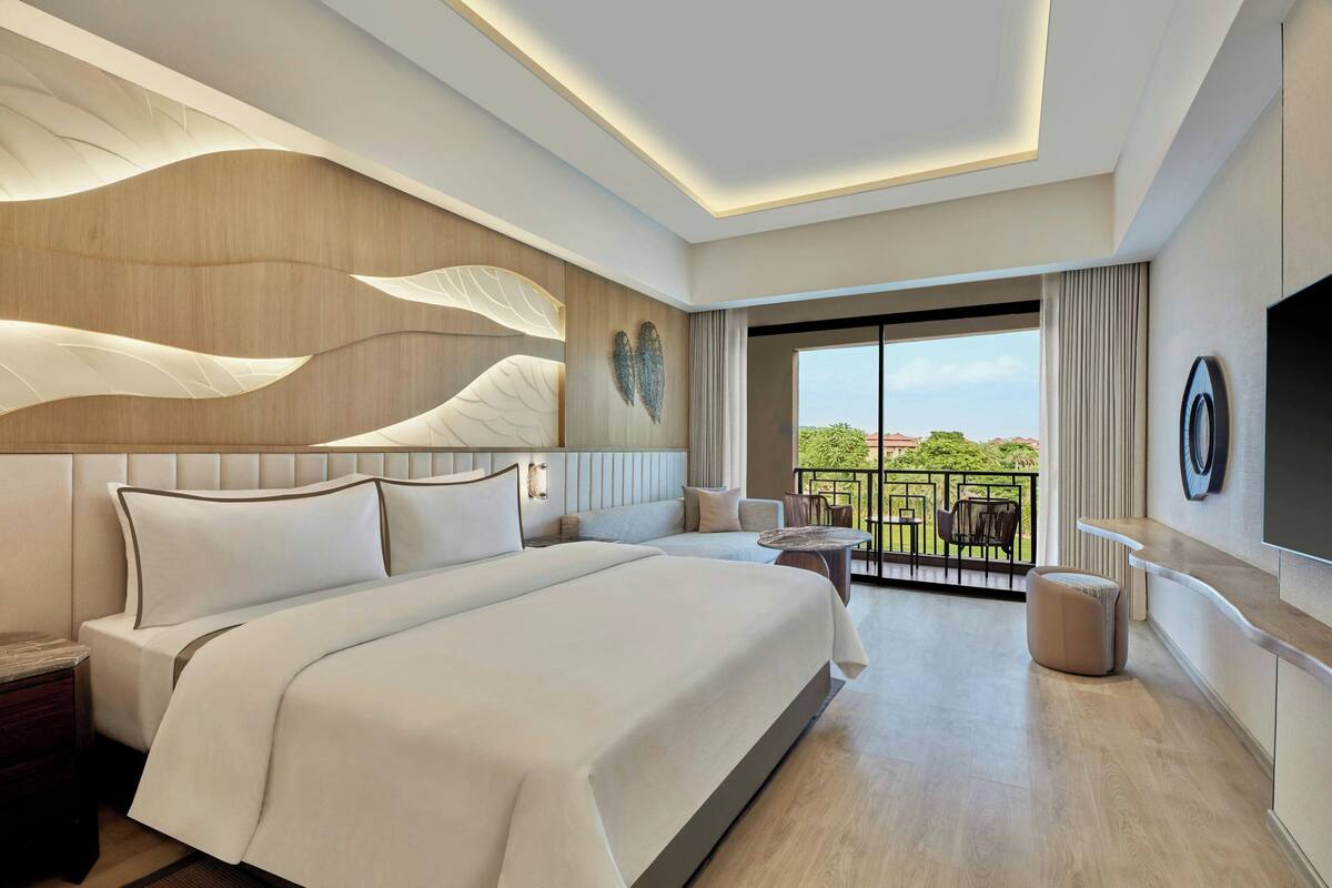 A modern hotel room with a large bed, a balcony with outdoor furniture, and a TV mounted on the wall.