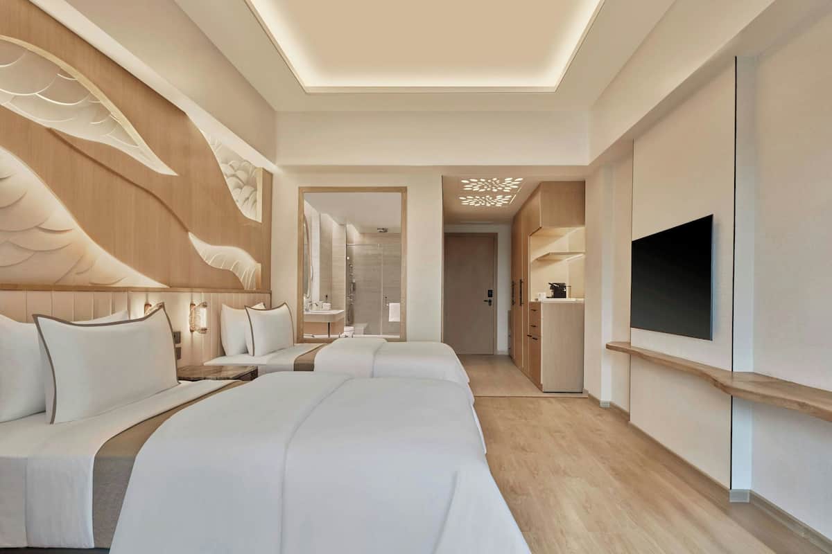 A modern hotel room with two large beds, a TV mounted on the wall, and a wooden ceiling design.