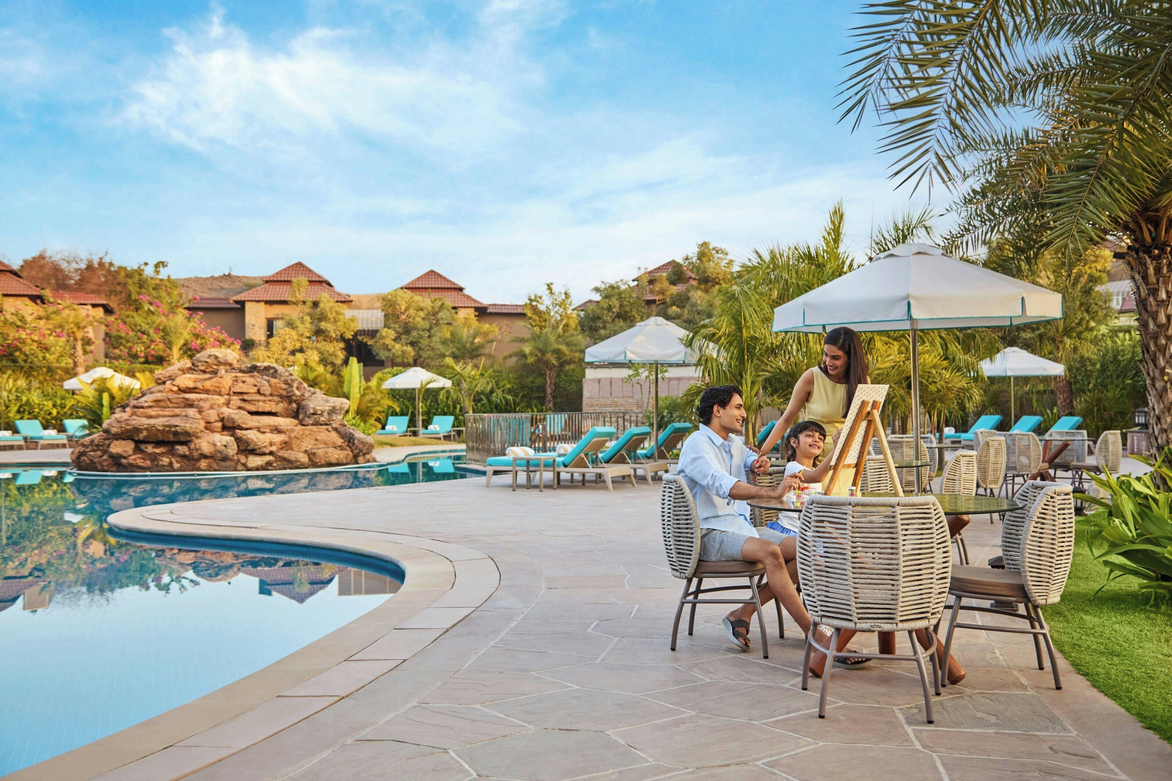 A poolside area with lounge chairs, a dining table, and a stone pathway leading to the pool.