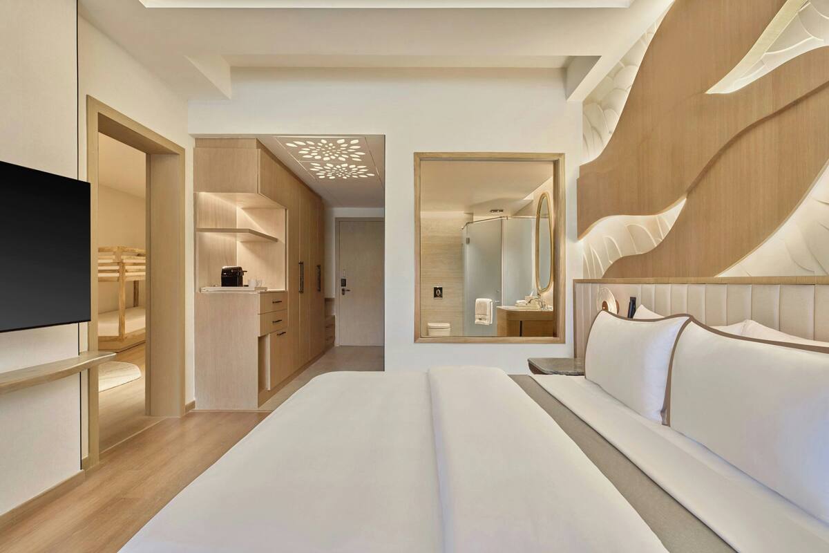 A modern hotel room with a large bed, a TV, a walk-in closet, and a bathroom with a mirror and vanity.