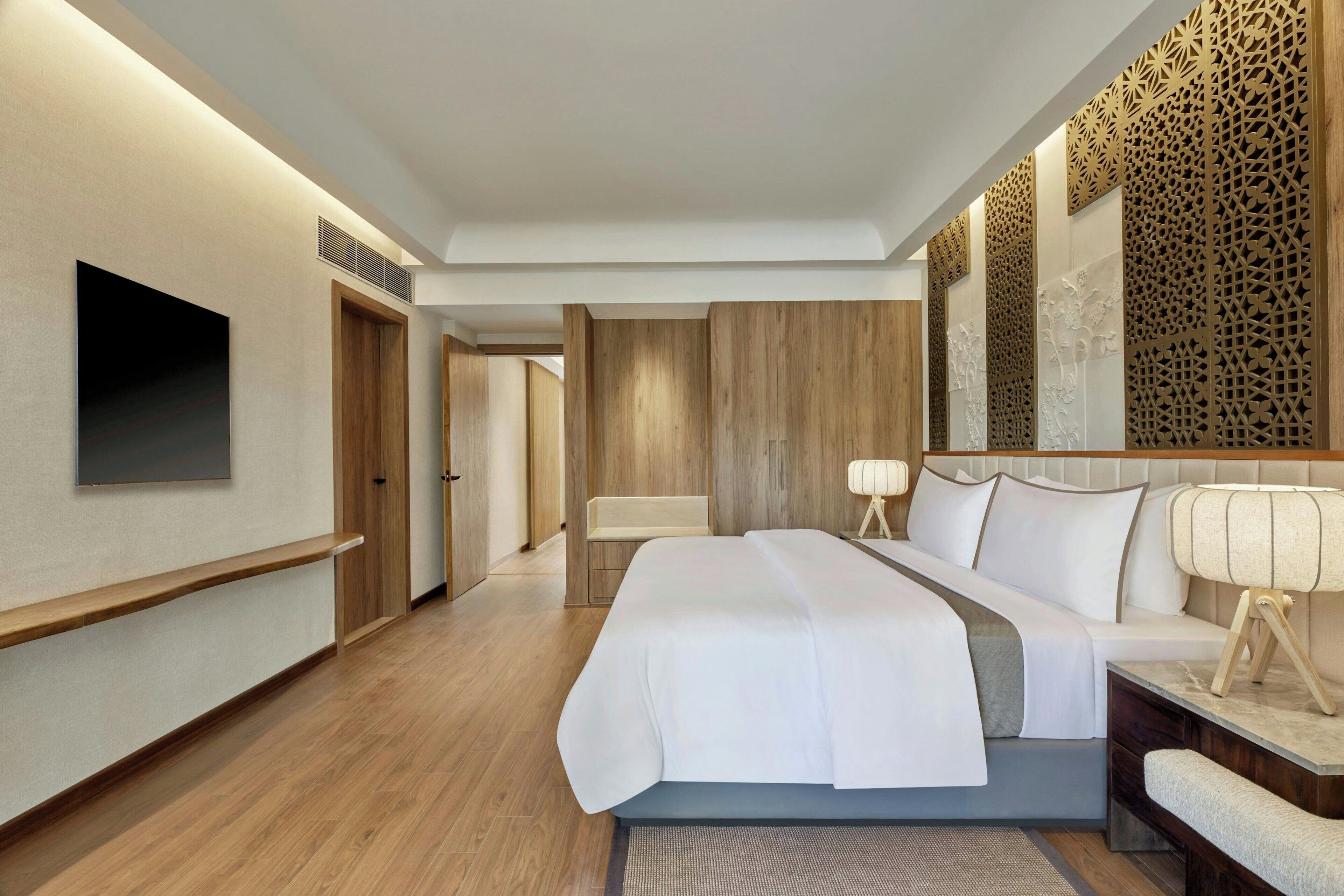 Una habitación de hotel moderna con una cama grande, un televisor de pantalla plana en la pared, un cabecero de madera y un panel decorativo.