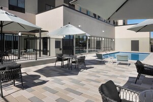 Un patio al aire libre con piscina, mobiliario y sombrillas.