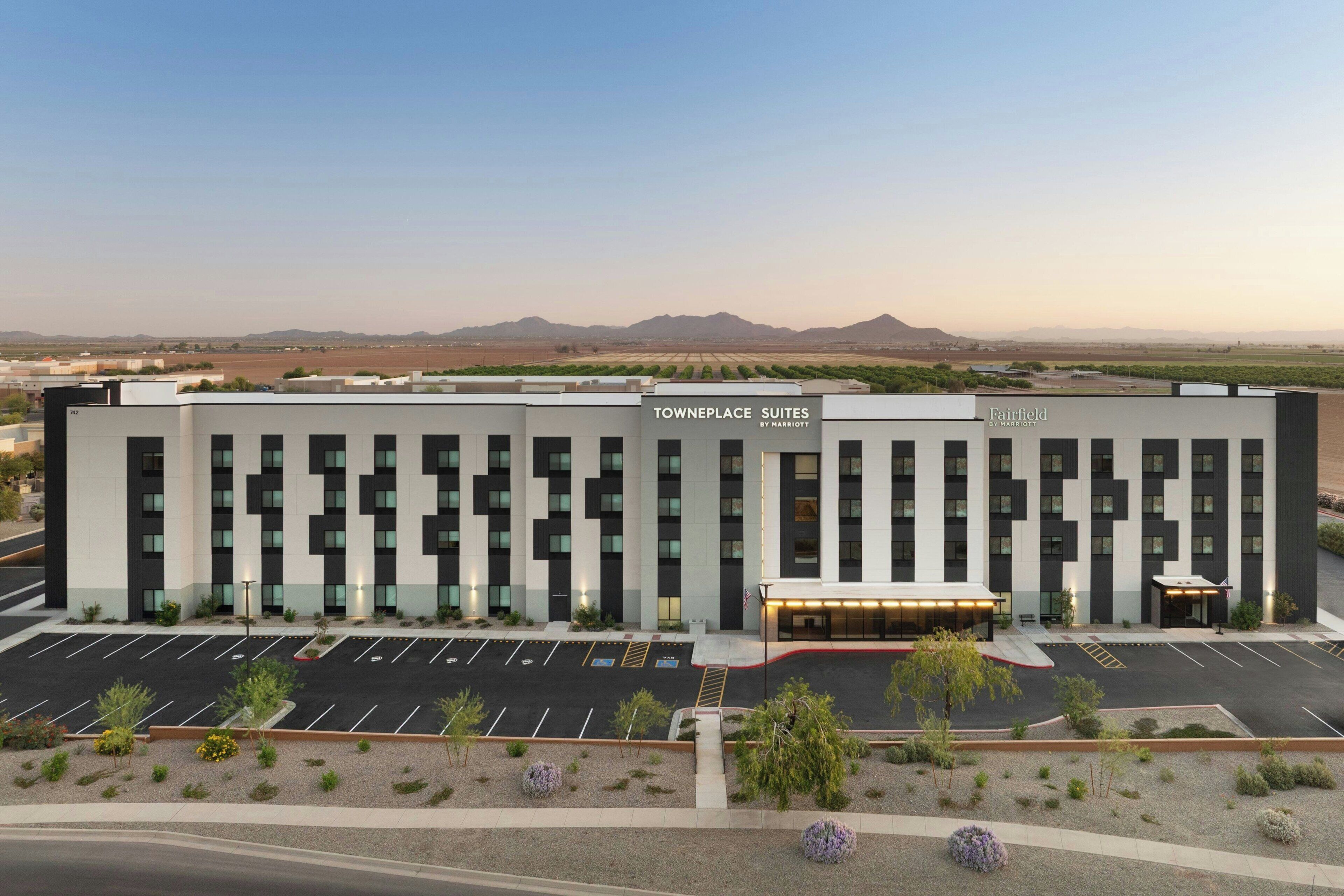 A modern hotel building with a parking lot and a view of distant mountains.
