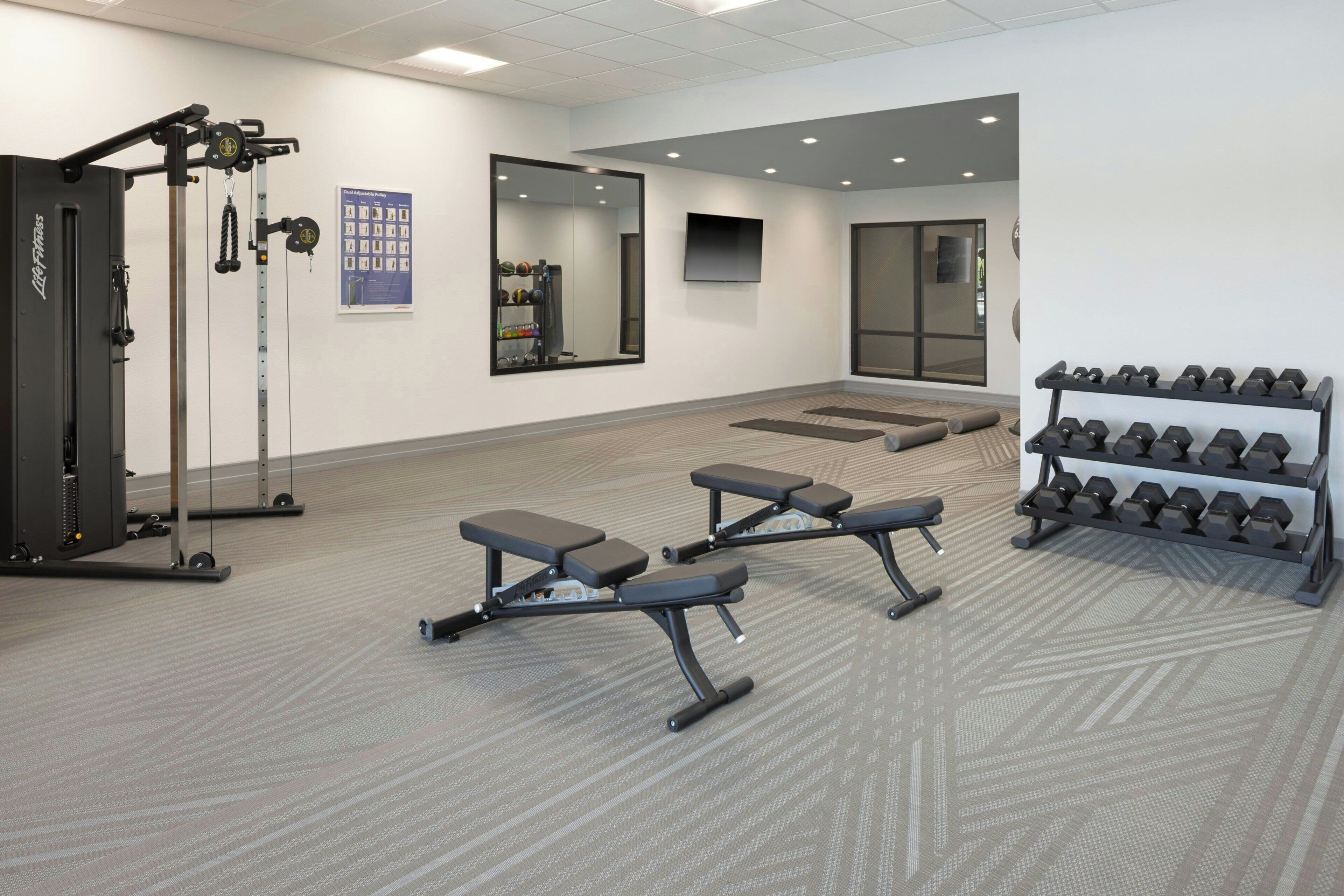 Un gimnasio con equipo de levantamiento de pesas, bancos y una barra de mancuernas.