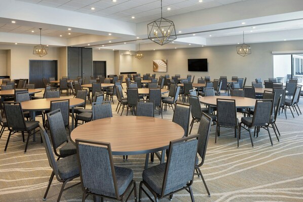 A large conference room with multiple tables and chairs, a flat-screen TV on the wall, and a geometric chandelier.