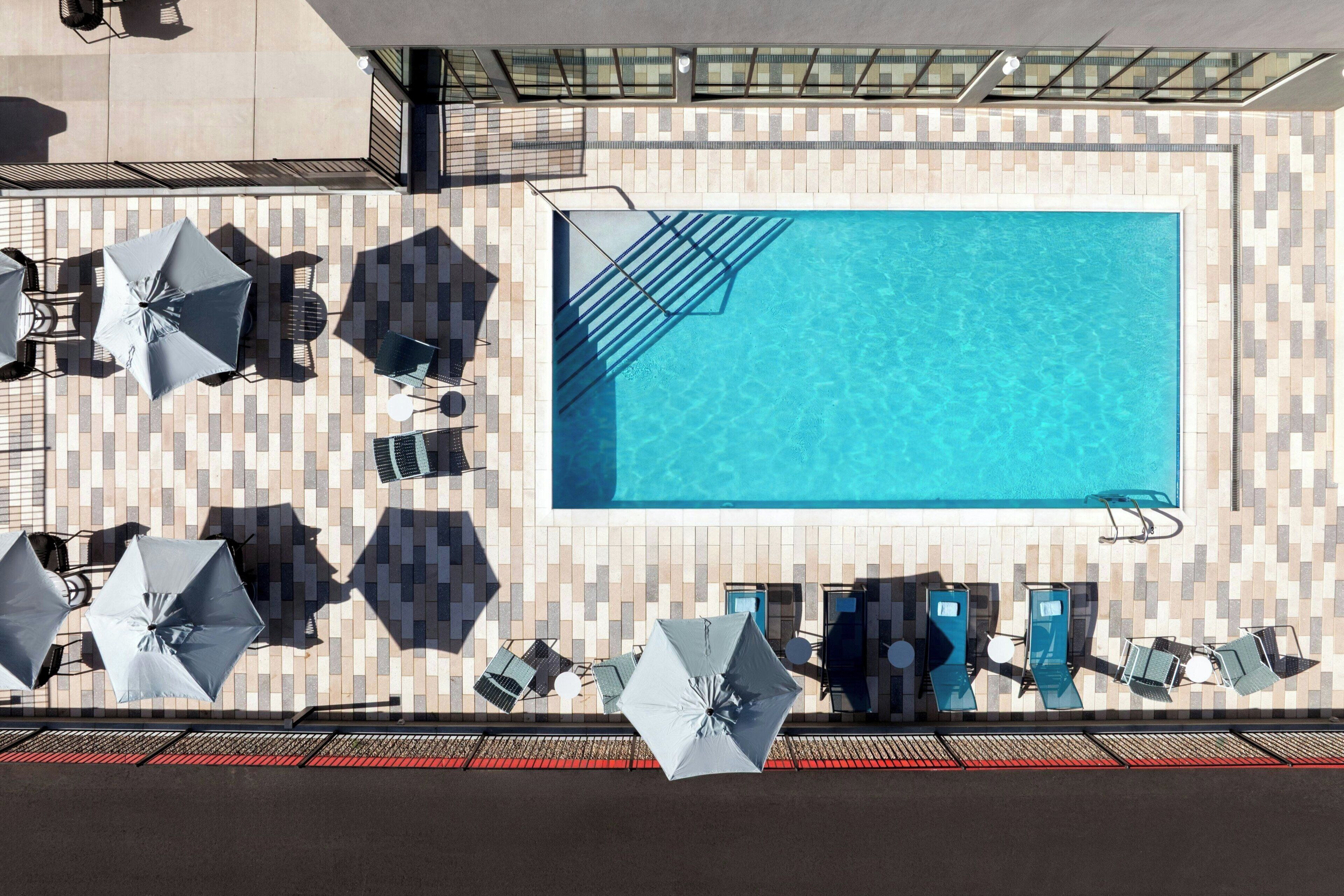 A rooftop swimming pool with a tiled deck, sun loungers, umbrellas, and a glass balustrade.