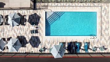 Una piscina sul tetto con solarium piastrellato, lettini, ombrelloni e balaustra in vetro.
