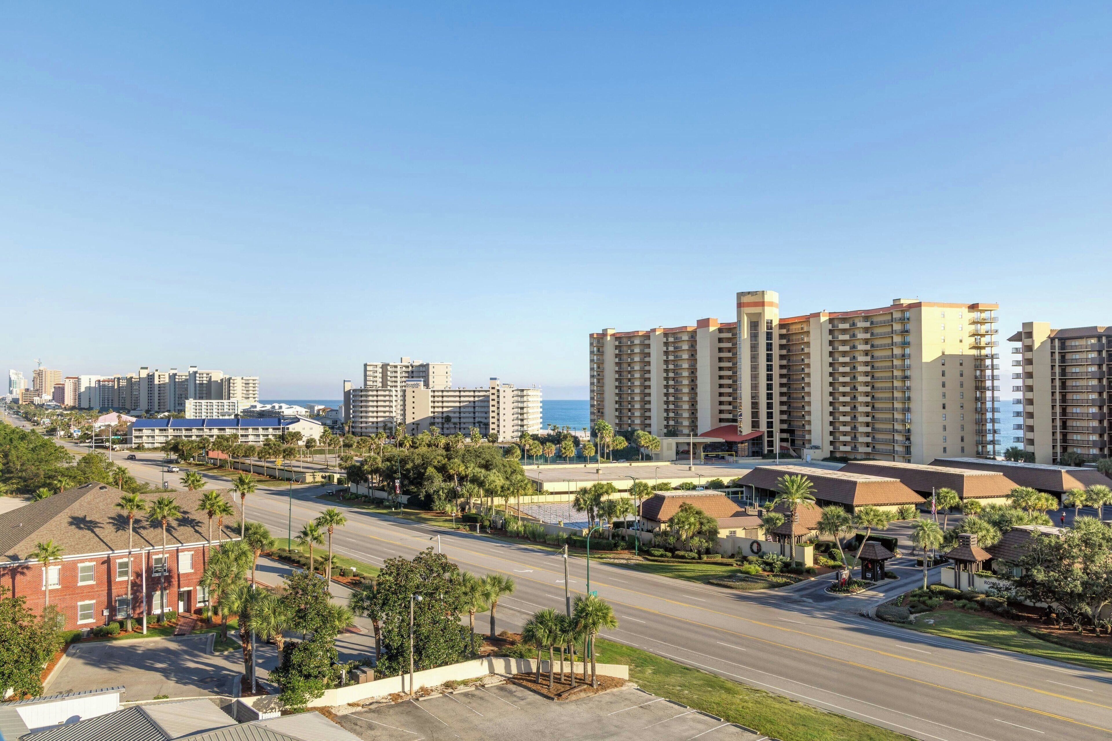 A coastal cityscape with high-rise buildings, a clear sky, and a road with palm trees.
