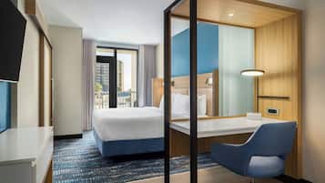 A hotel room with a bed, a desk, a chair, a TV, and a large window with a view of buildings.