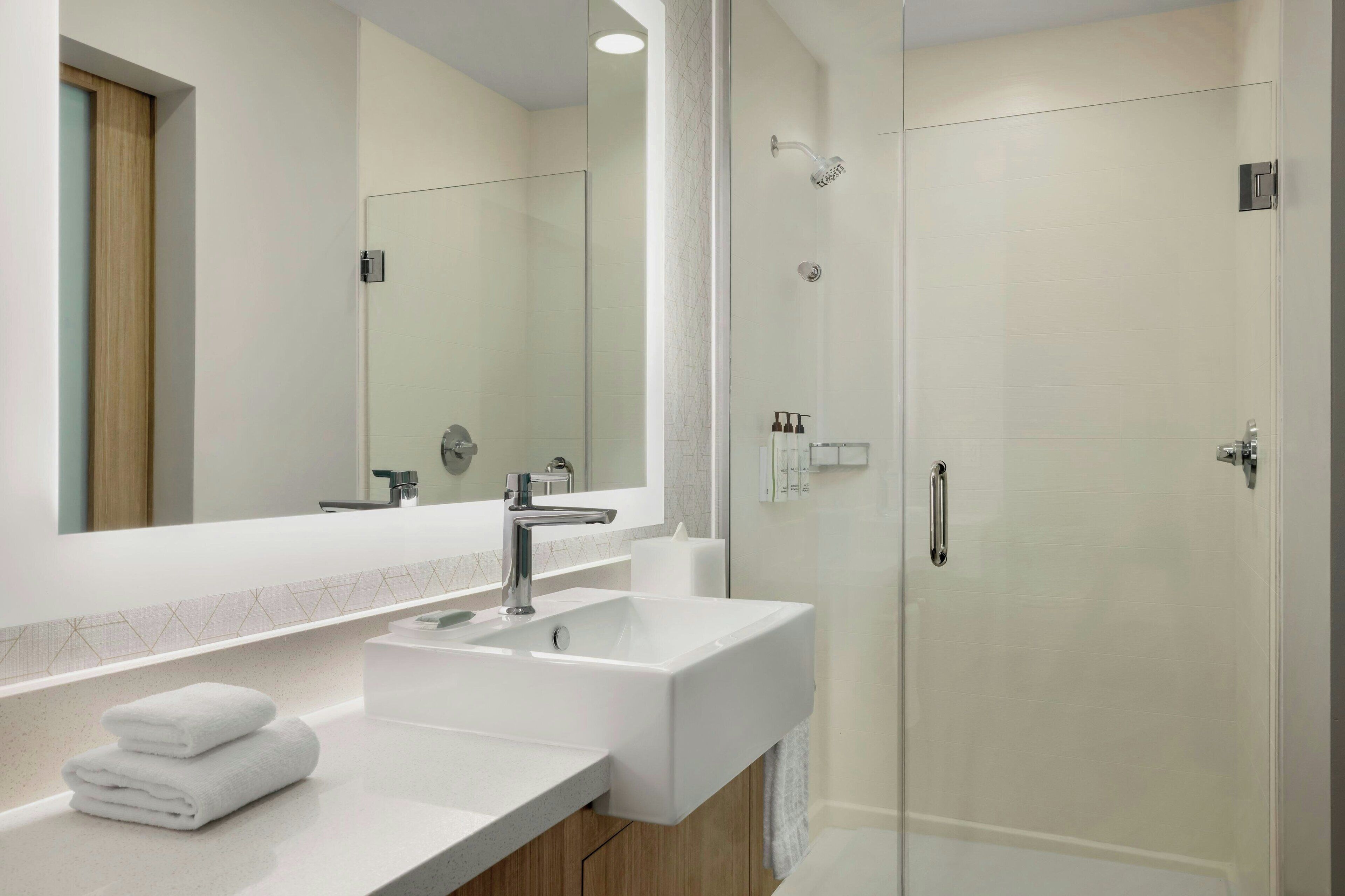 A modern bathroom with a large mirror, two sinks, and a glass-enclosed shower.