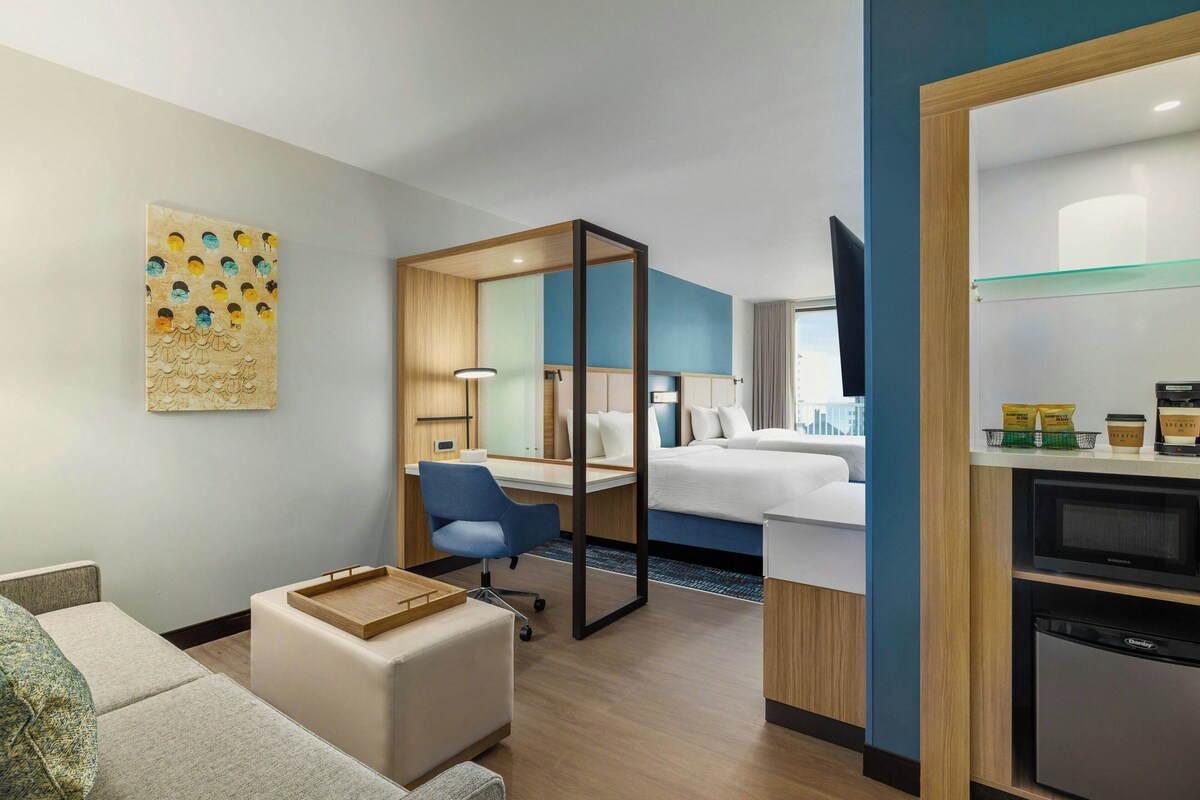 Ein Hotelzimmer mit Bett, Schreibtisch, Stuhl, kleinem Tisch, Fernseher und Mikrowelle.