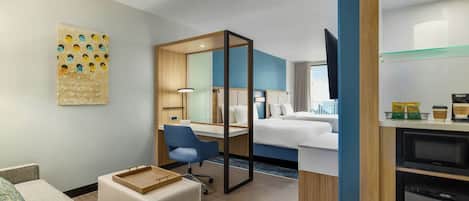 Habitación de hotel con cama, escritorio, silla, pequeña mesa, televisor y microondas.