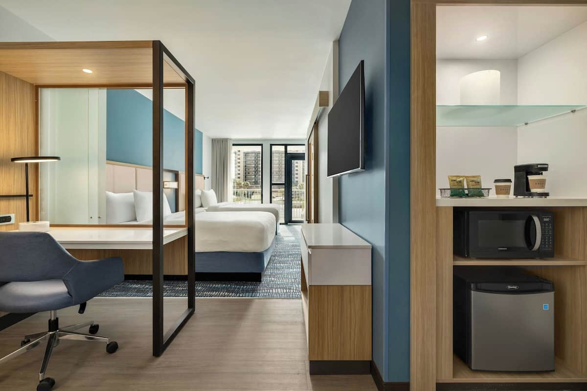 Une chambre d’hôtel équipée d’un lit, d’un bureau, d’une chaise, d’une télévision, d’un four à micro-ondes, d’un réfrigérateur et offrant une vue sur les bâtiments.