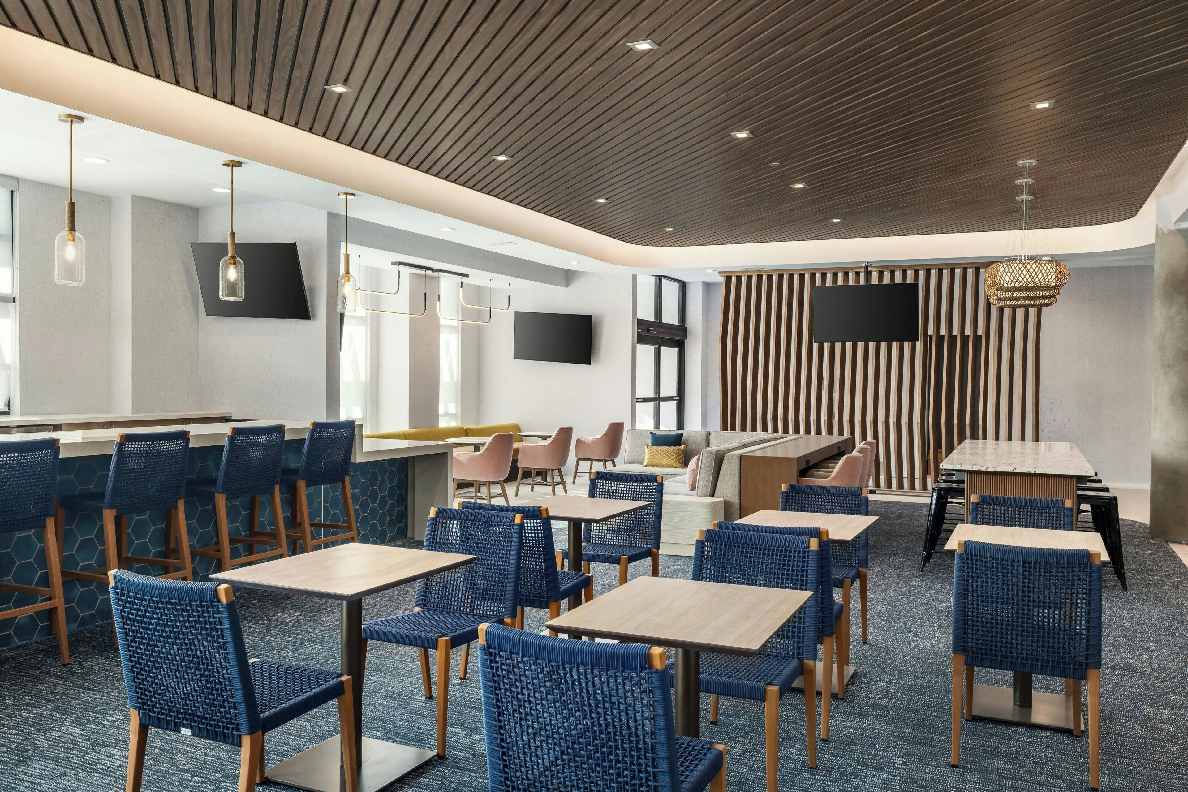 Un restaurante moderno con sillas de ratán azul, mesas de madera y techo de madera.