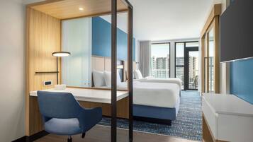 A hotel room with a desk, chair, bed, and large windows offering a city view.