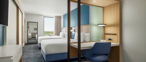 Ein Hotelzimmer mit Bett, Schreibtisch, Stuhl, Fernseher und einem durch eine offene Tür einsehbaren Badezimmer.