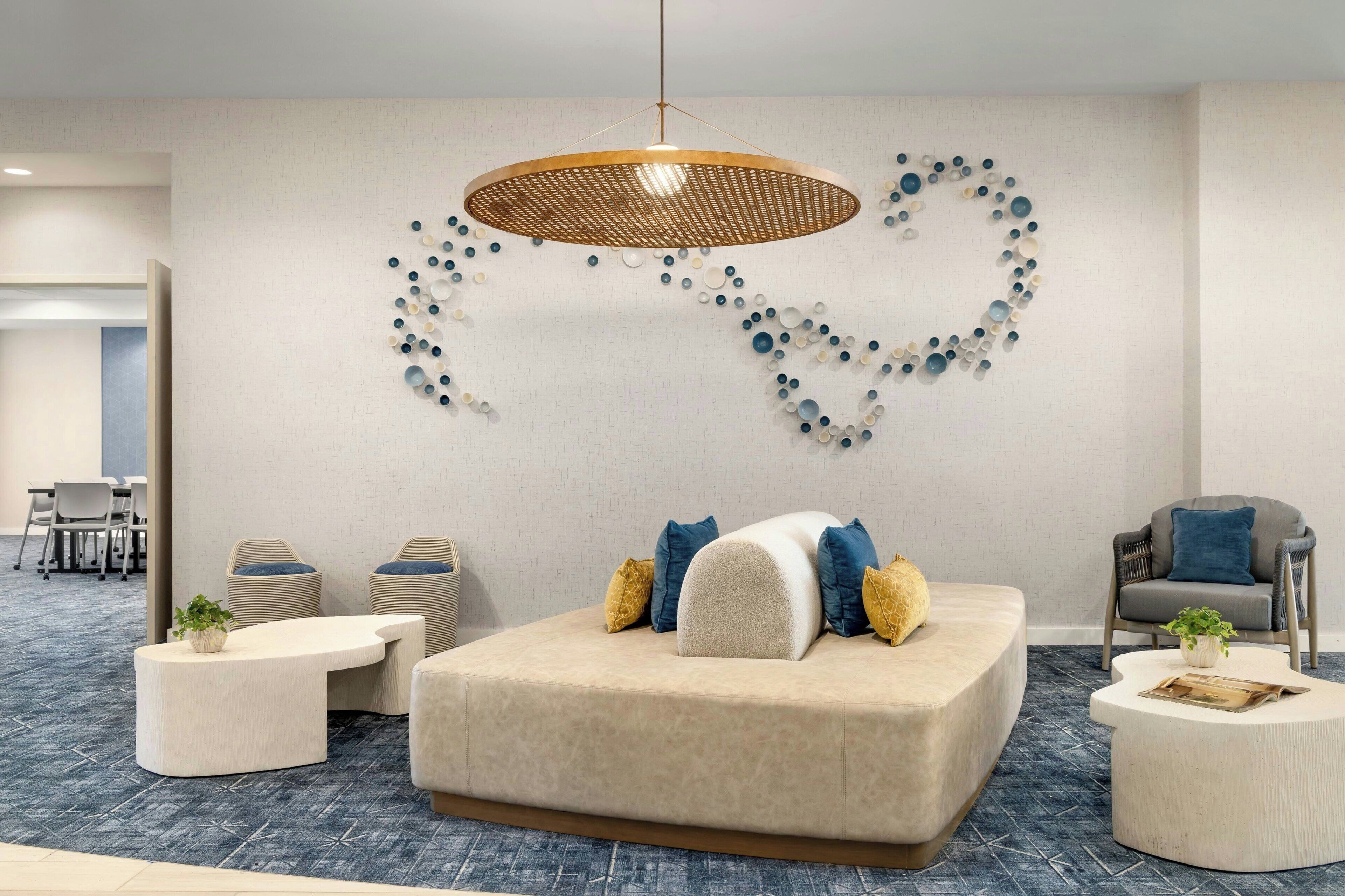 Un espace de détente moderne comprenant un canapé, deux petites tables d’appoint, un luminaire suspendu et une œuvre d’art murale.