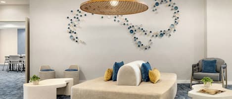Un espace de détente moderne comprenant un canapé, deux petites tables d’appoint, un luminaire suspendu et une œuvre d’art murale.