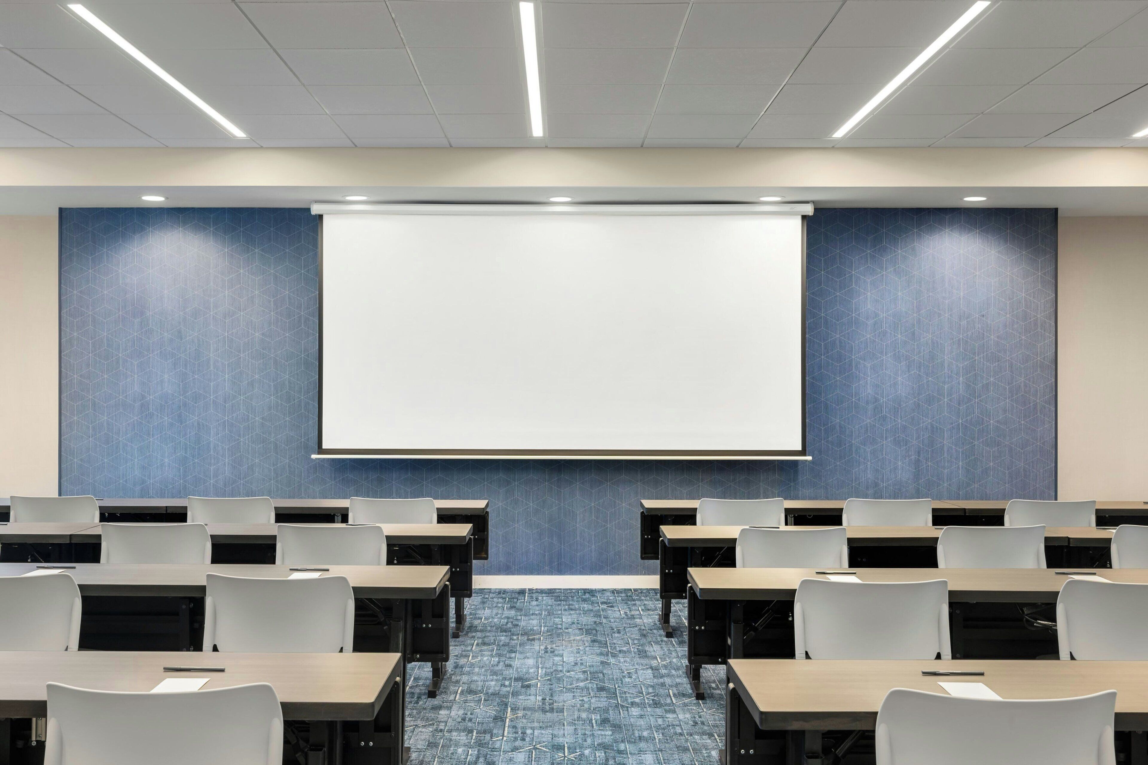 A conference room with a large screen, rows of tables, and chairs.