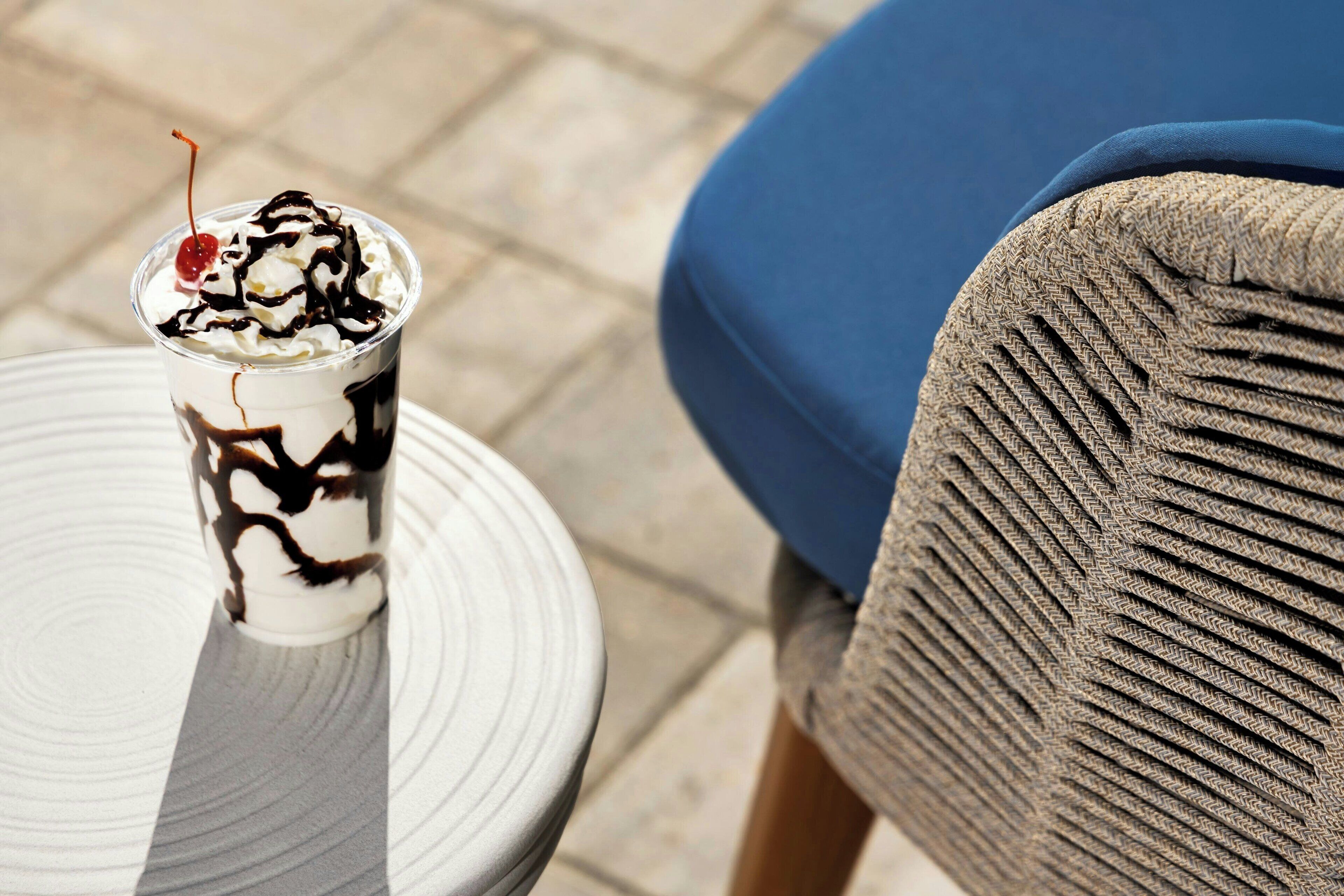 Un postre en un vaso sobre un plato blanco, una silla azul y una tela con textura.