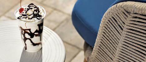 Un postre en un vaso sobre un plato blanco, una silla azul y una tela con textura.