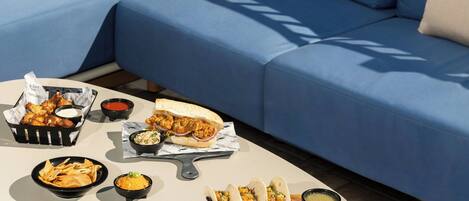 A dining table with various food items including tacos, nachos, and a sandwich, set on a patio with a blue sofa in the background.