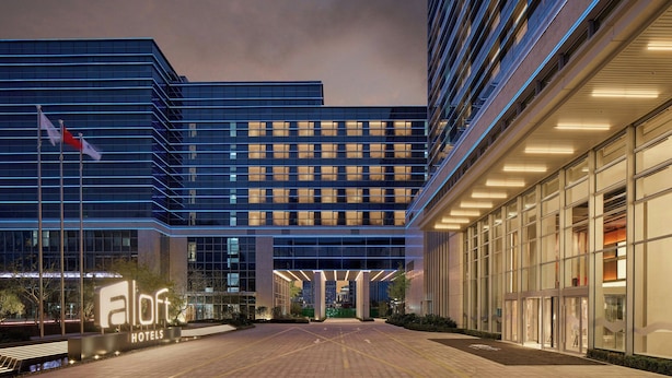 A modern hotel building with a prominent entrance, large windows, and a well-lit facade. - Aloft Shanghai Hongqiao (Shanghai)
