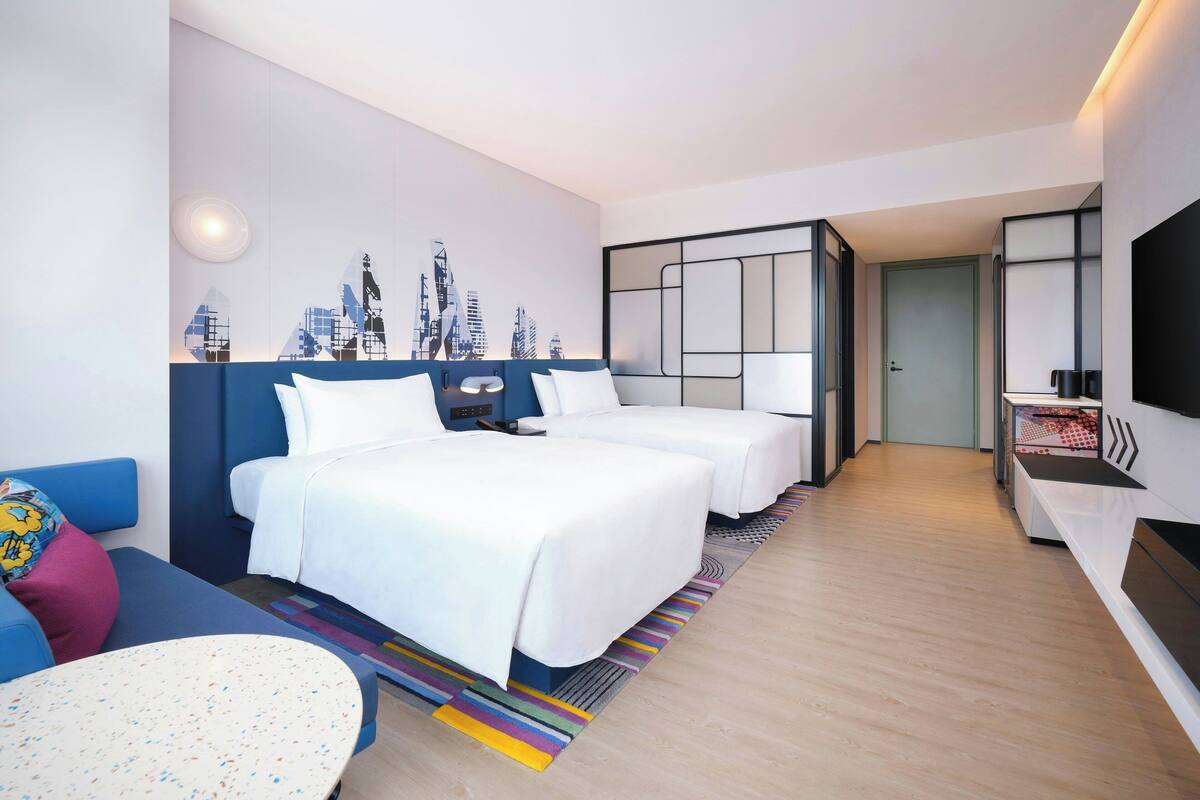 A hotel room with two beds, a sofa, a small table, and a cityscape wall art.