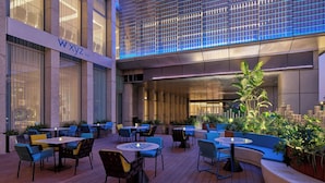An outdoor seating area with tables and chairs, a bar sign, and potted plants. - Aloft Shanghai Hongqiao (Shanghai)