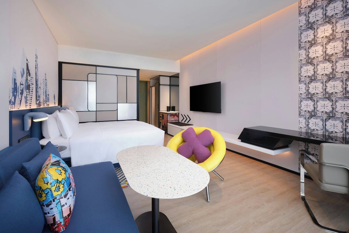 A modern hotel room with a bed, a desk, a chair, and a TV.