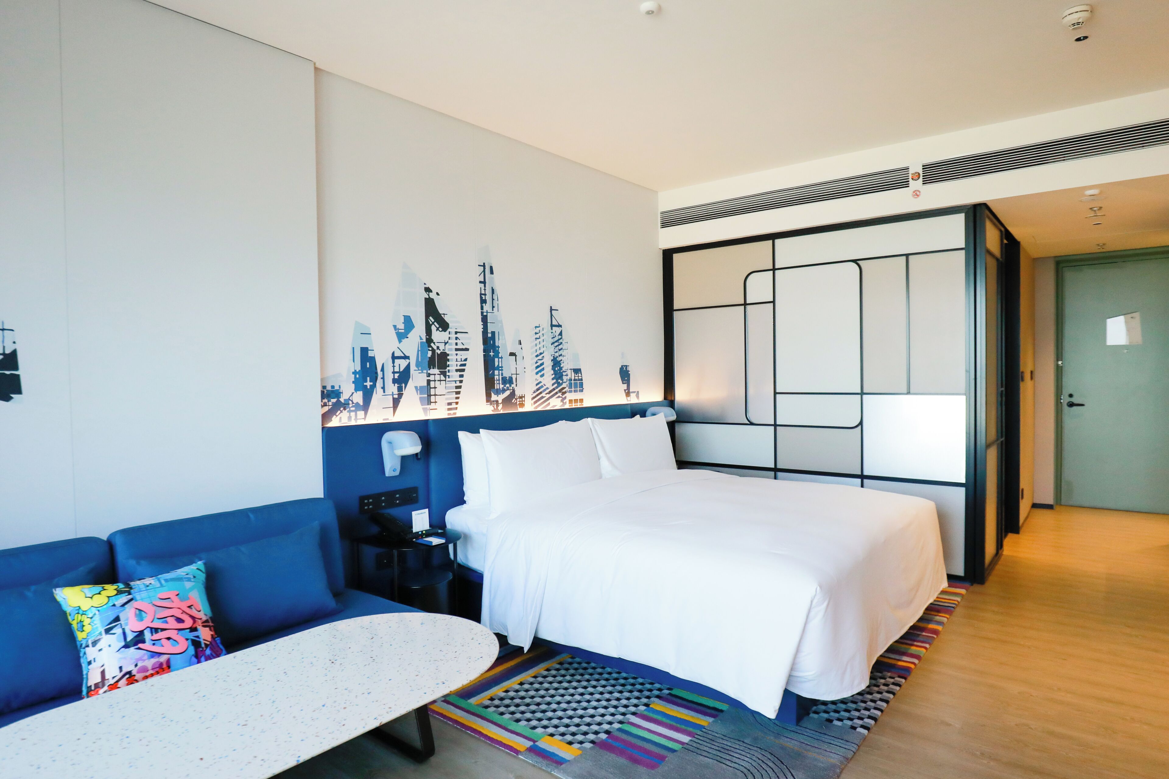 Una habitación de hotel con una cama, un sofá azul, una mesita y una alfombra colorida.