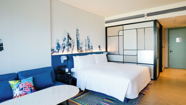 Una habitación de hotel con una cama, un sofá azul, una mesita y una alfombra colorida.