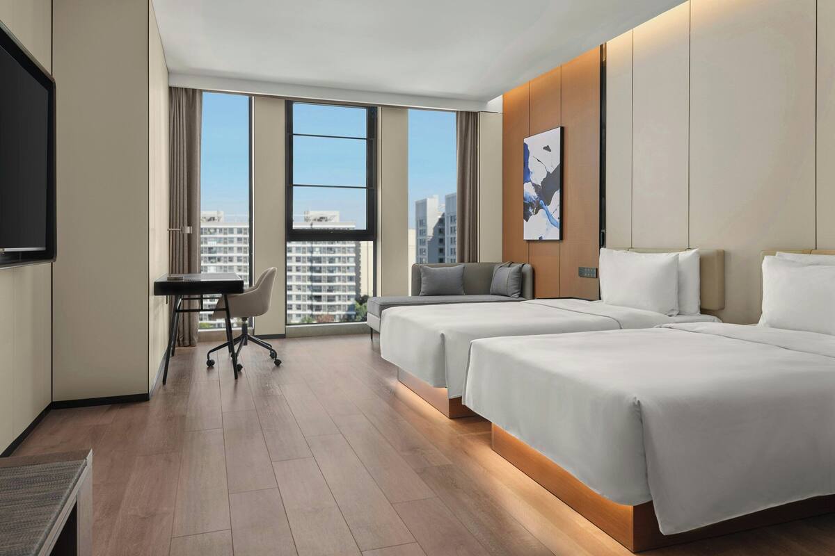 Una habitación de hotel moderna con dos camas, un escritorio y un ventanal que ofrece vistas a la ciudad.