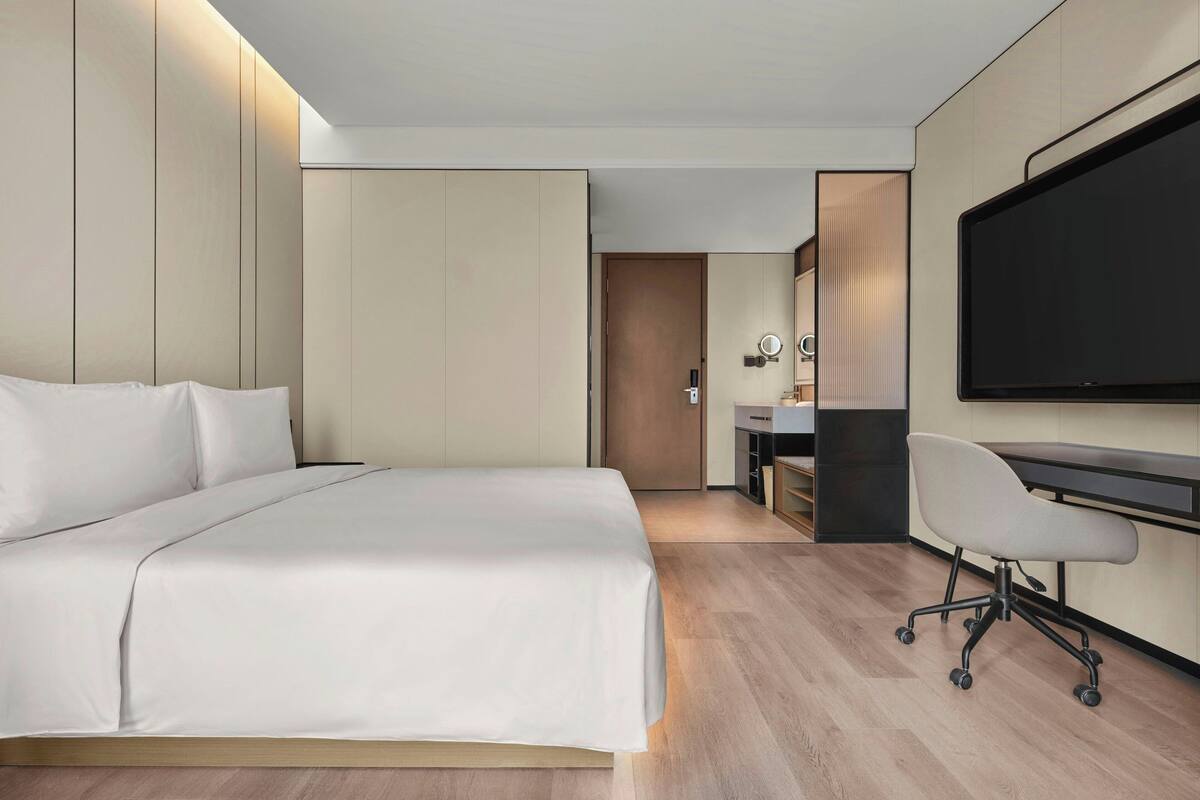 Habitación de hotel moderna con una cama grande, un escritorio con silla, televisión de pantalla plana y vestidor.