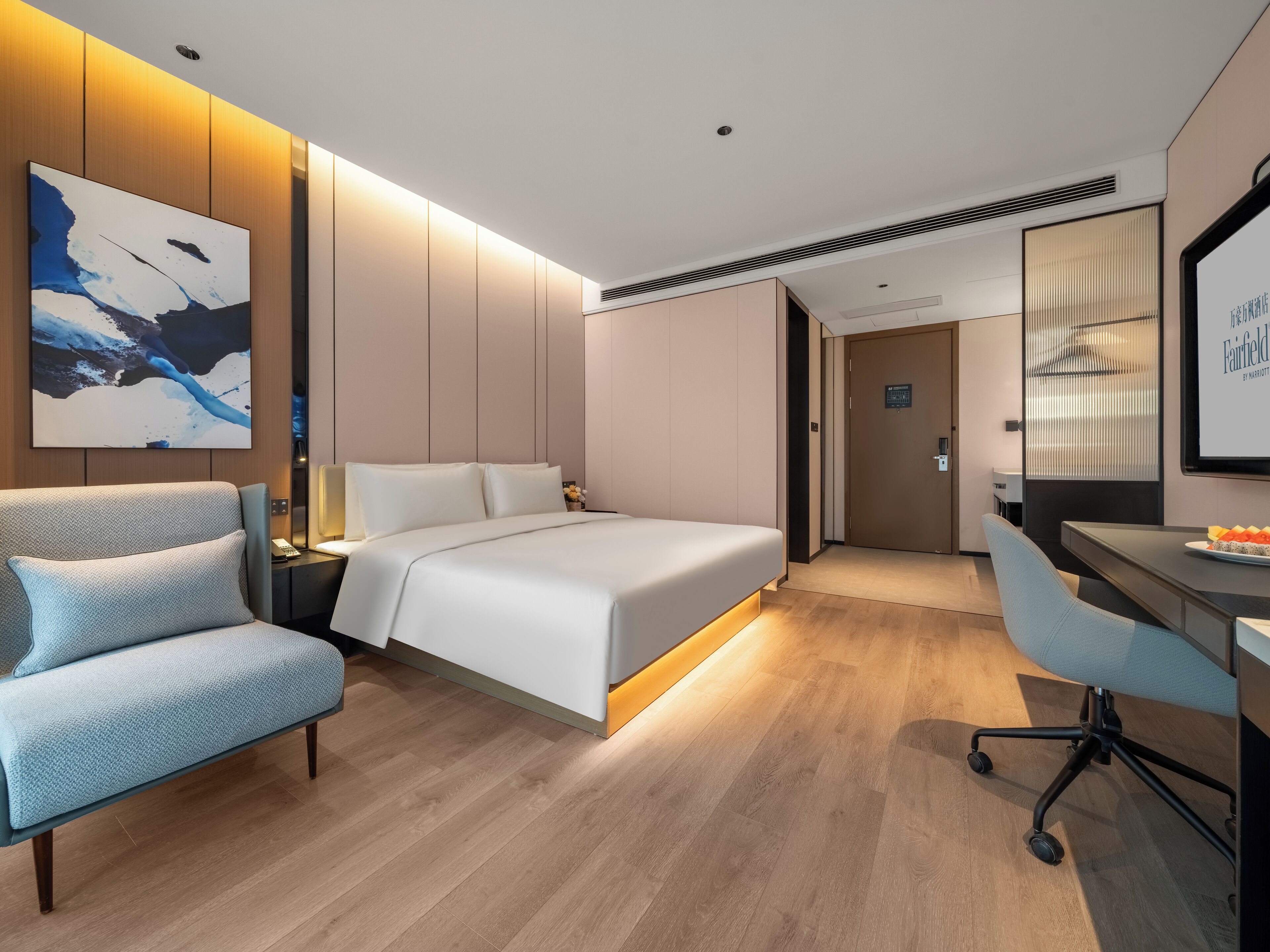 A modern hotel room with a bed, a desk, a chair, and a large abstract painting on the wall.