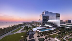 A modern hotel with a glass facade, a swimming pool, and a view of a bridge and mountains in the background. - Courtyard By Marriott Xiamen Xiang’An (Xiamen)