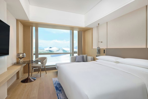 A modern hotel room with a large bed, a desk with a chair, a flat-screen TV, and a large window offering a view of the city. - Courtyard By Marriott Xiamen Xiang’An (Xiamen)
