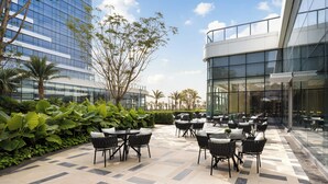 Un espace extérieur aménagé en terrasse, avec des tables et des chaises, entouré de verdure et de bâtiments modernes.